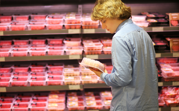 Mann liest in der Fleischabteilung das Rückseitenetikett auf einer Fleischverpackung durch 