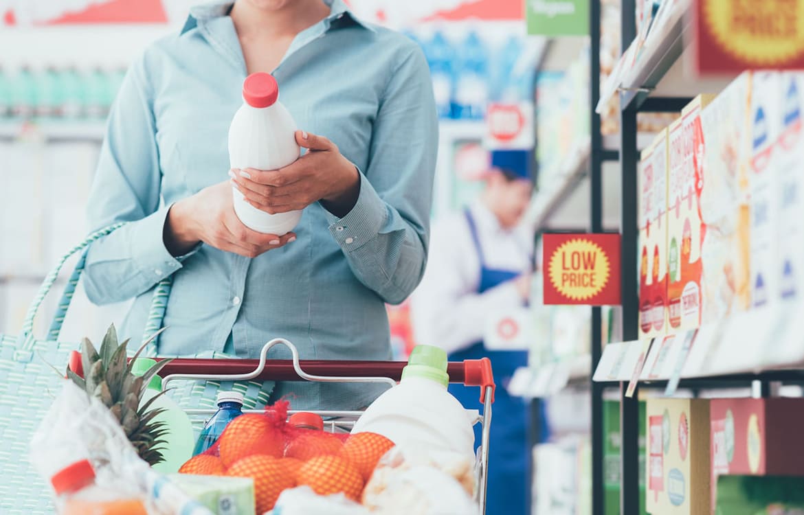 Frau liest Lebensmittelkennzeichnung auf Milchflasche im Supermarkt