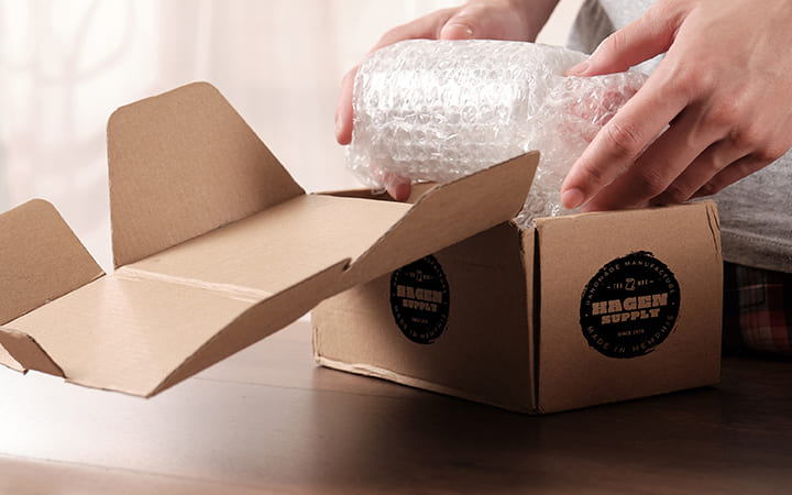 Frau packt Produkt in Faltschachtel Frau packt Produkt in Faltschachtel