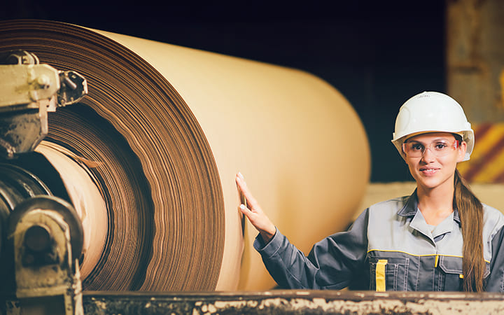 Frau steht neben Testlinerpapier-Rolle Frau steht neben Testlinerpapier-Rolle