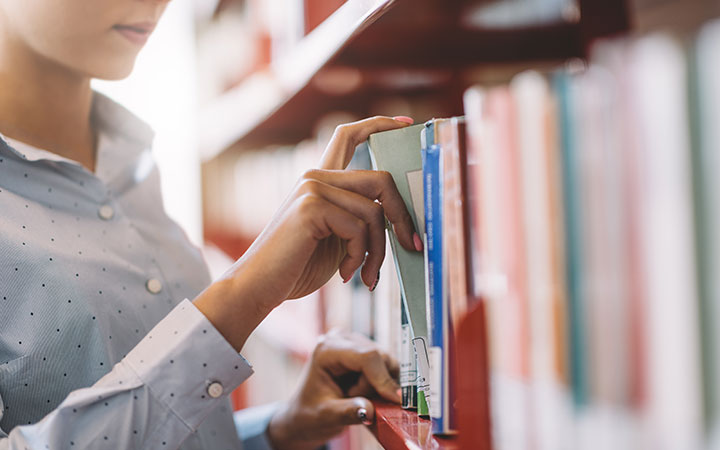 Frau nimmt Buch aus Bücherregal raus